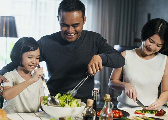 Father, mother, and daughter making a salad in their home.